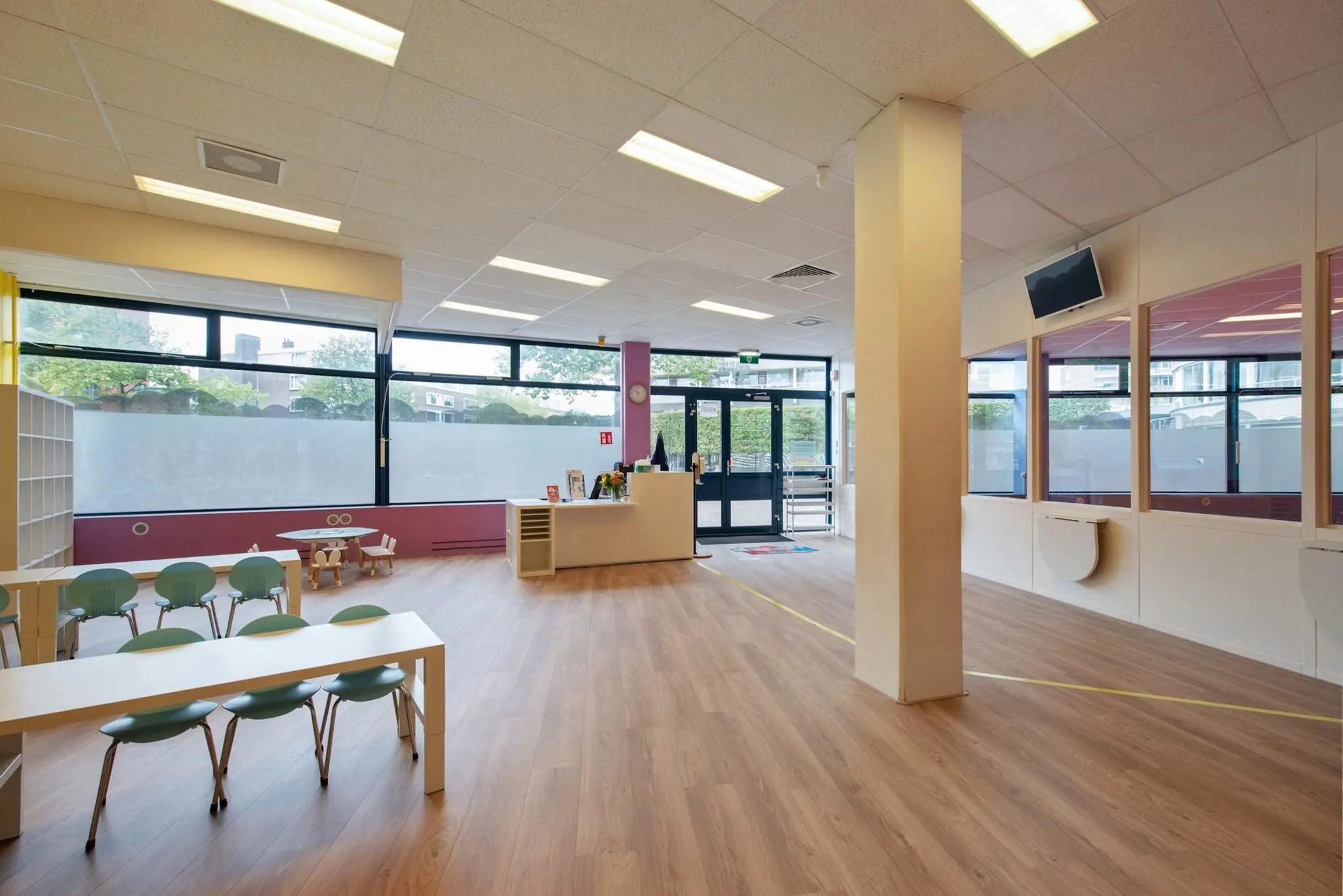 Moderne en lichte wachtruimte of binnenruimte in een kinderopvang aan de Koningin Julianalaan, met speelhoek, kinderstoelen en balie.